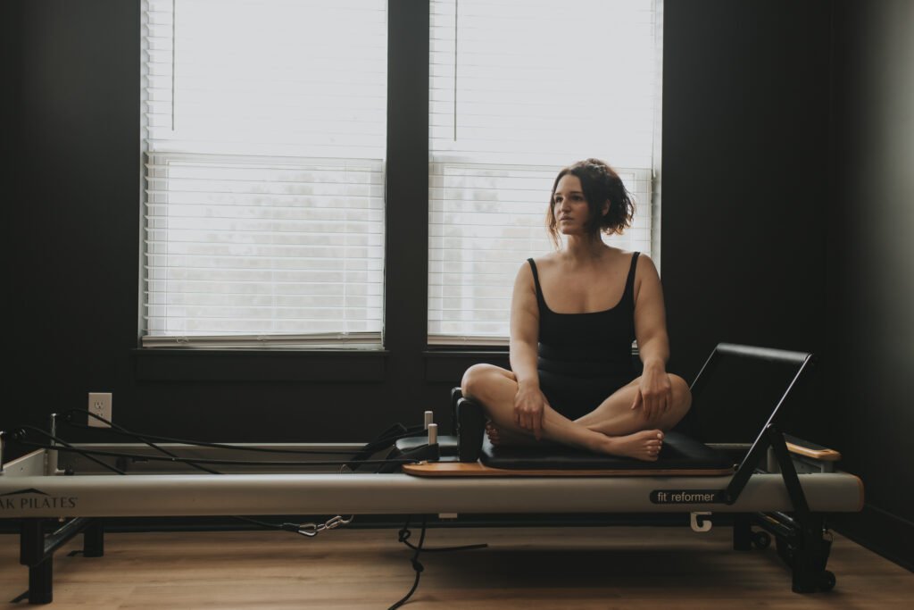 Woman sitting on a Pilates reformer machine looking to the right. 